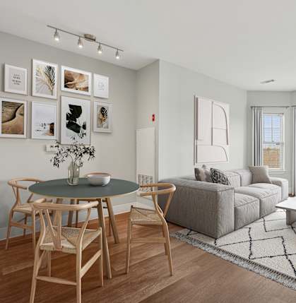 A living room with a grey couch, a round table with chairs, and pictures on the wall.