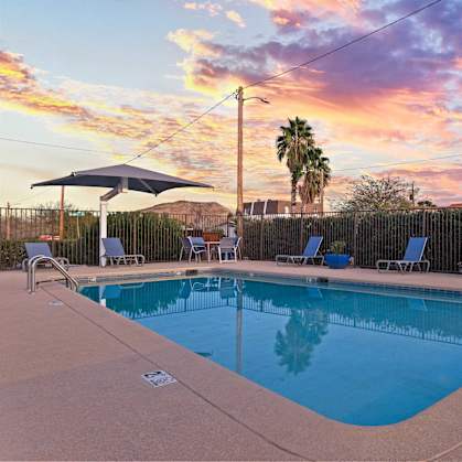 A pool surrounded by chairs and a fence with a sunset in the background.
