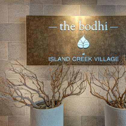 a sign for the booth at island creek village with two plants in front of it at The Bodhi at Island Creek Village, Duxbury