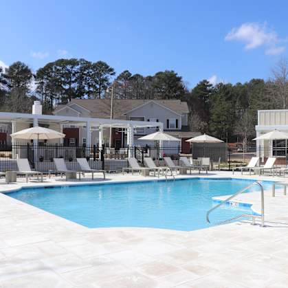 A large swimming pool surrounded by lounge chairs and umbrellas at Carlton Park Apartment Homes, MS, 39232