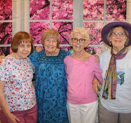 Four women are standing together in front of a floral backdrop.