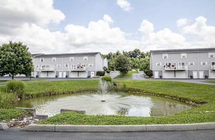 a fountain sits in the middle of a pond in front of apartment buildings