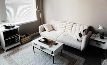 A white couch with a pillow and a blanket on it sits in a living room.