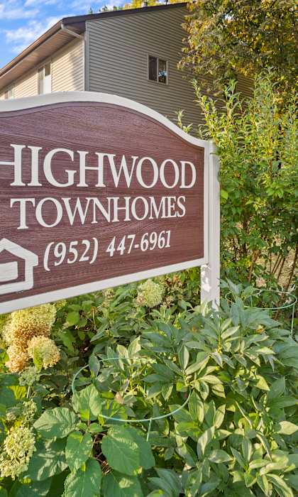 A sign for Highwood Townhomes stands in front of a building and some trees.