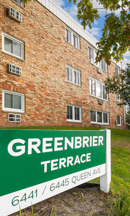 A sign for Greenbrier Terrace stands in front of a brick building.