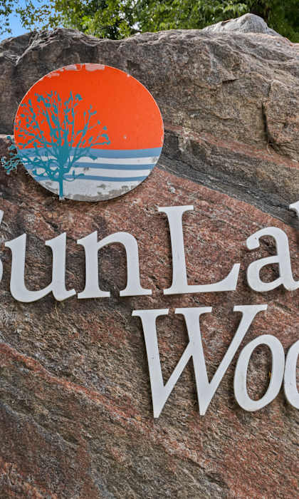 A sign for Sun Lake Woods with a tree logo on top.