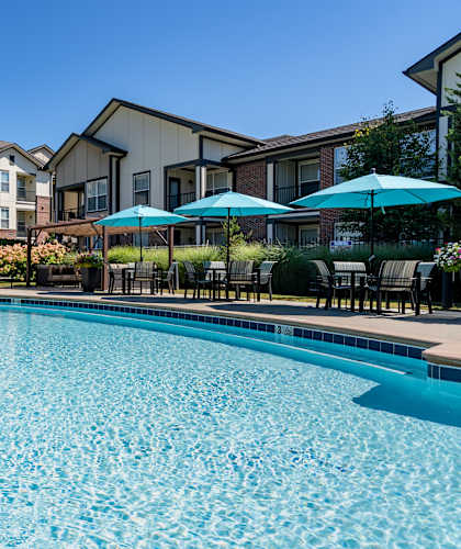 A swimming pool surrounded by apartment buildings and lounge chairs.