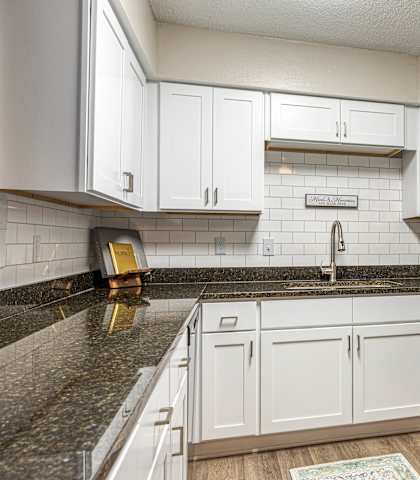 A kitchen with white cabinets and a black granite countertop.