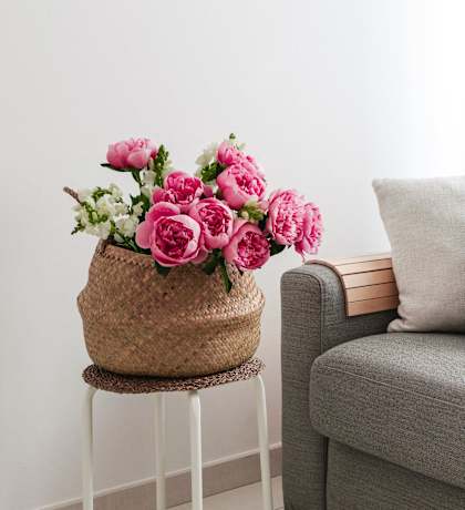 A grey couch with a black pillow and a basket of pink flowers.