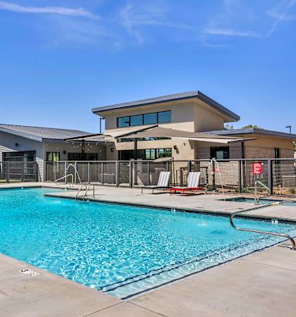 A large swimming pool with red lounge chairs and a building in the background.