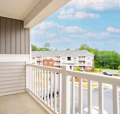 A balcony with a white railing and a view of a parking lot and buildings.