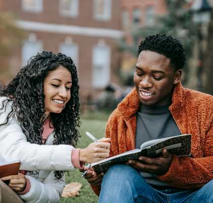 a man and woman sitting on the grass reading a book