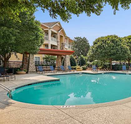 A large swimming pool surrounded by trees and chairs.