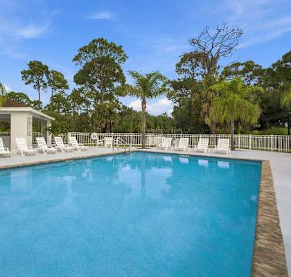A pool surrounded by white chairs and trees.