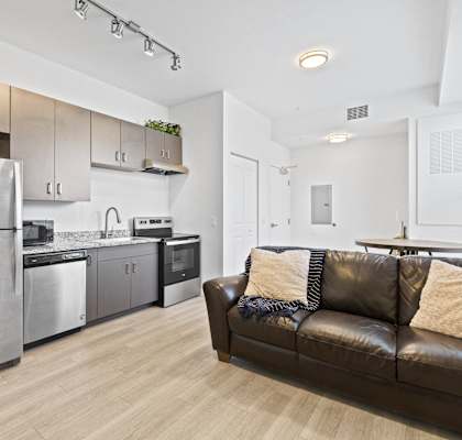 a living room with a leather couch and a kitchen with stainless steel appliances