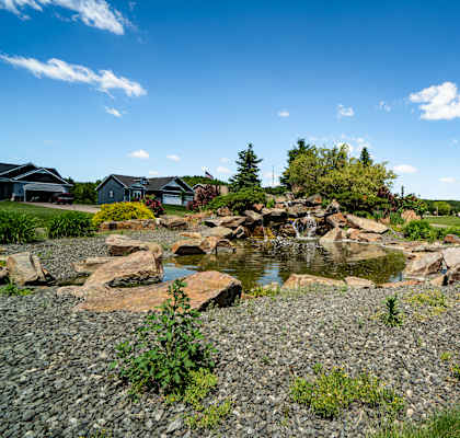 A small pond with rocks in the foreground and houses in the background.