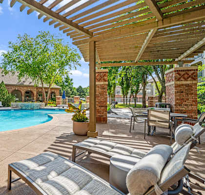 A pool area with a pergola and lounge chairs.