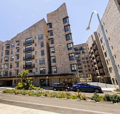 A modern building with curved balconies and a parking lot in front.