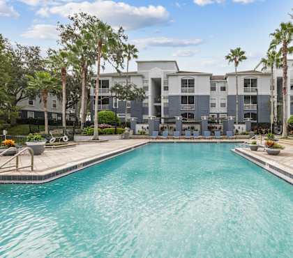 A swimming pool in front of a building surrounded by palm trees.