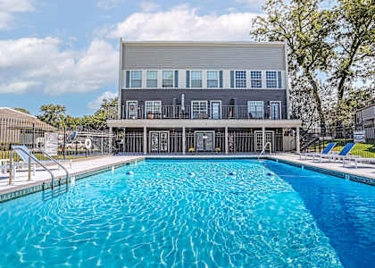 A large swimming pool in front of a grey building with a white fence around it.