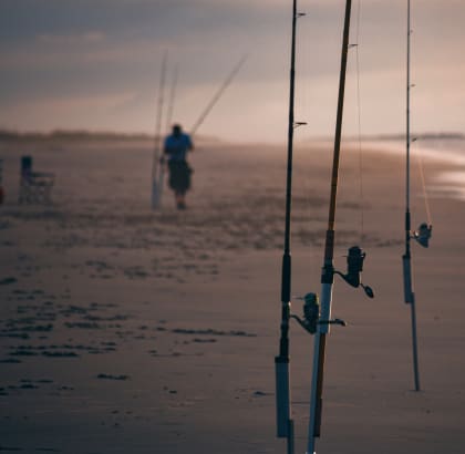 two fishing poles on the beach with a person standing in the distance