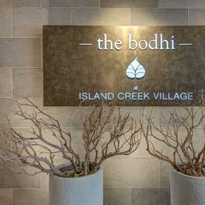 a sign for the booth at island creek village with two plants in front of it at The Bodhi at Island Creek Village, Duxbury