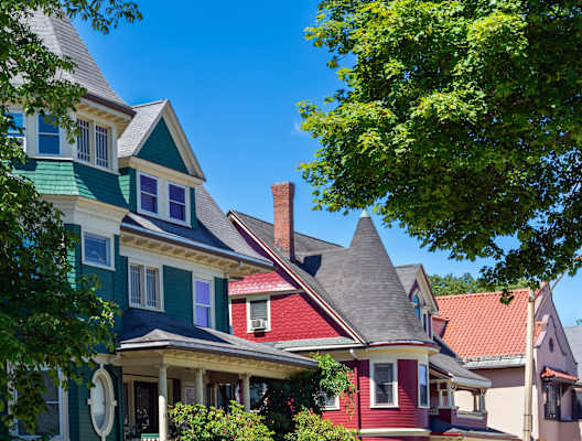 A row of colorful houses with green trees in front.