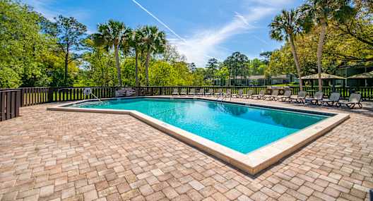 a swimming pool with chairs and trees in the background