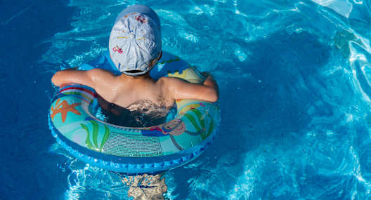 A person in a swimming pool wearing a swim cap and floatation ring.