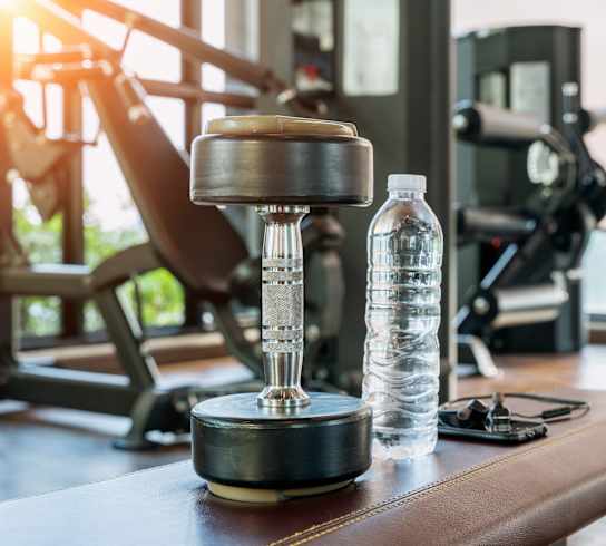A bottle of water and a dumbbell on a bench in a gym.