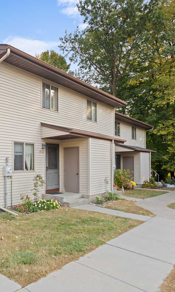 A beige two-story apartment building with a brown roof and a small front yard.