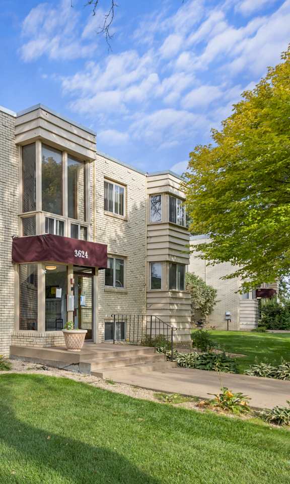 the front of a brick apartment building with green grass and trees
