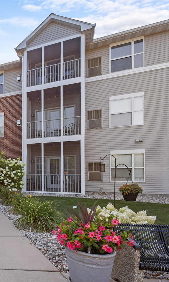 The image shows a sunny day at the entrance of apartment building I045 with a walkway and flower pots on either side.