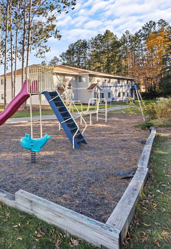 A playground with a slide and swings in a grassy area.