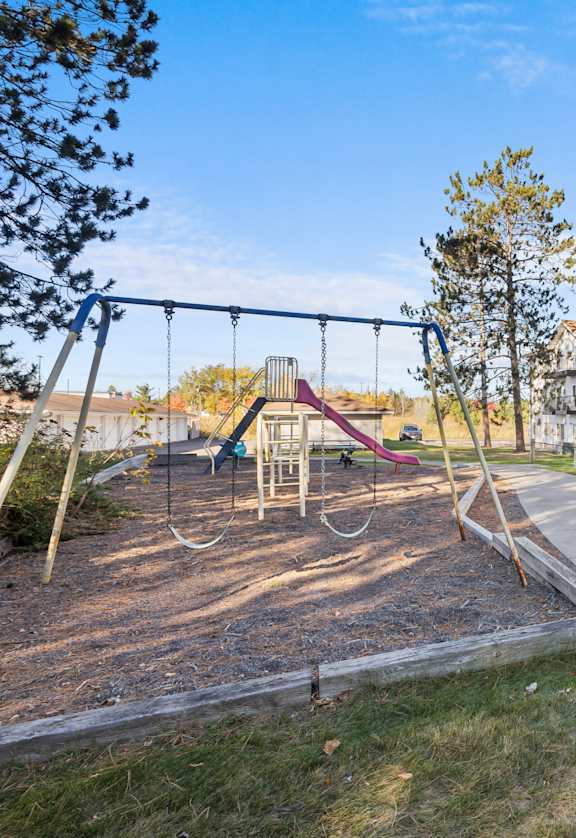 A playground with a swing set and a building in the background.