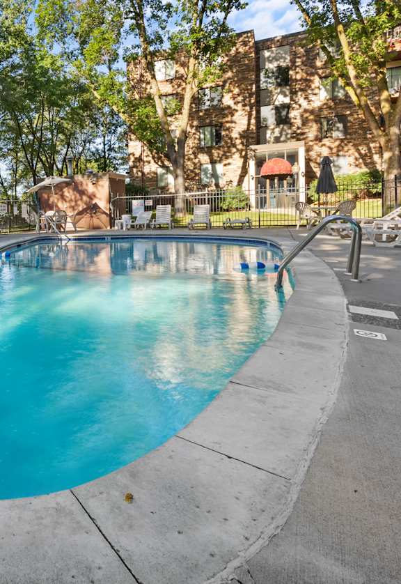 A swimming pool surrounded by trees and chairs.