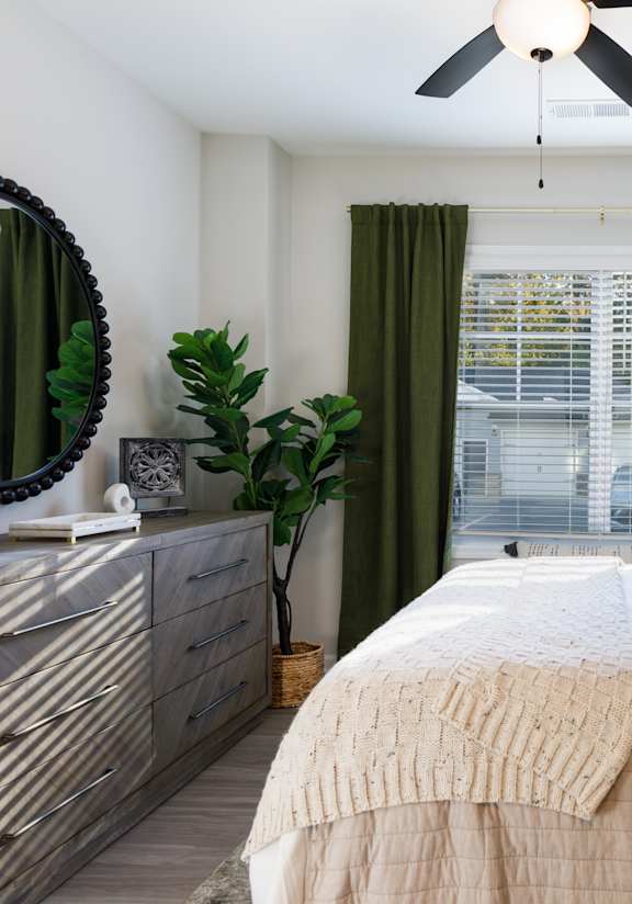 A bedroom with a bed, dresser, mirror, and plants.