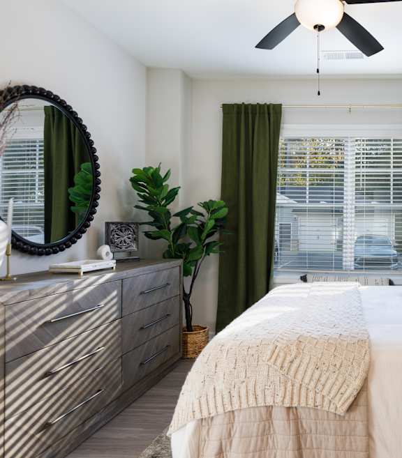 A bedroom with a bed, dresser, mirror, and plants.