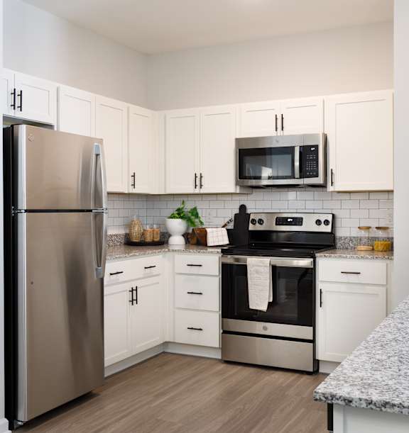 A kitchen with a refrigerator, microwave, oven, and sink.