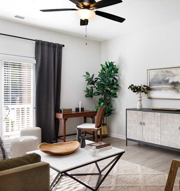A living room with a ceiling fan, a chair, a table, a cabinet, and a painting on the wall.
