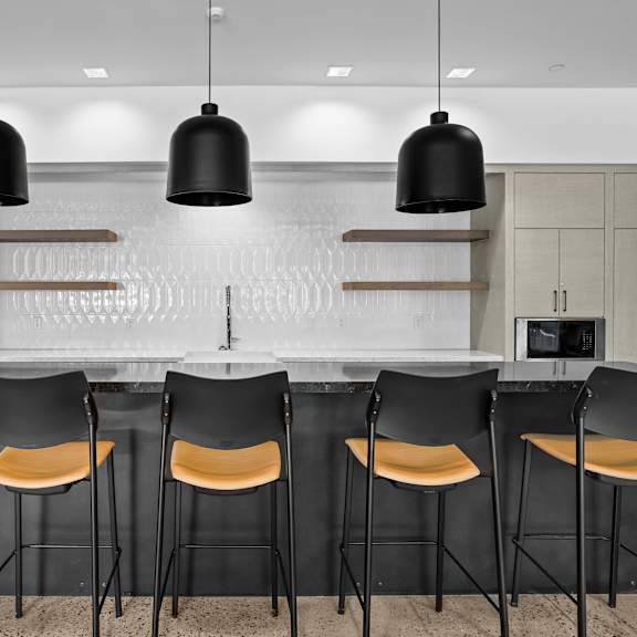 A modern kitchen with black chairs and a white backsplash.