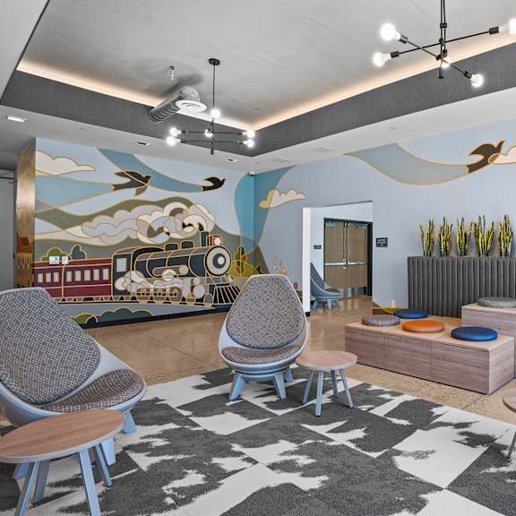 A room with a mural of a train and clouds on the wall, a radiator, and a patterned rug on the floor.