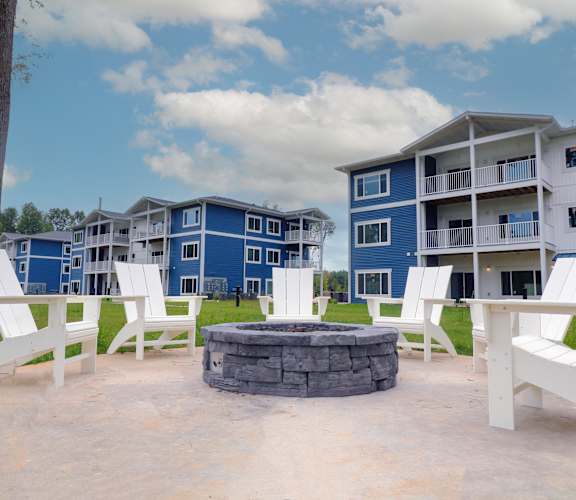 our fire pit is in front of our blue apartments with white chairs and benches