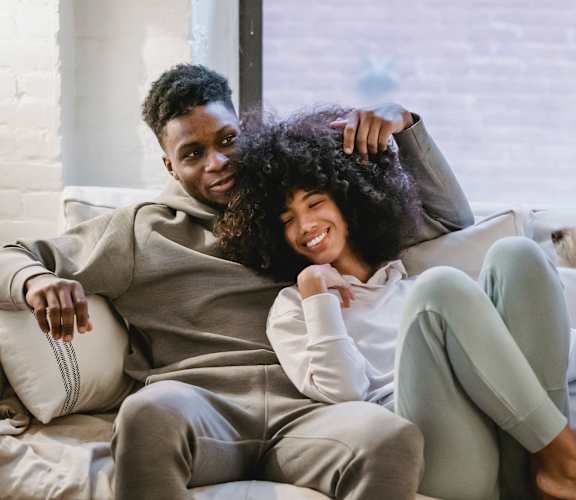 A man and woman are sitting on a couch with a dog beside them.