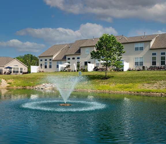 A fountain in the middle of a pond in front of a row of houses.