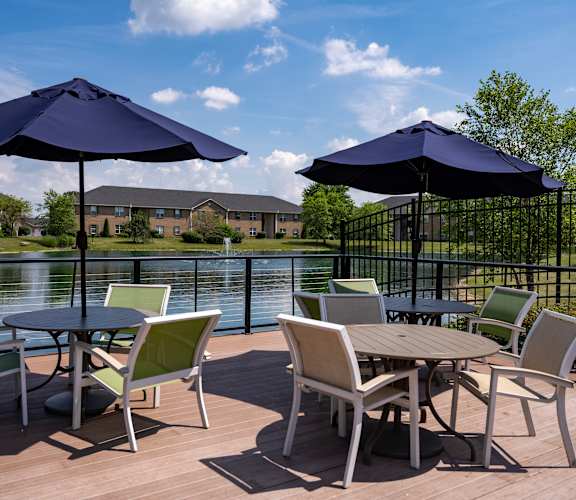A table with chairs and umbrellas on a deck overlooking a lake.