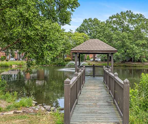 A wooden pier leads to a gazebo over a lake surrounded by trees.