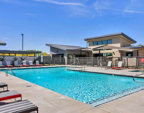 A large swimming pool with red lounge chairs and a building in the background.