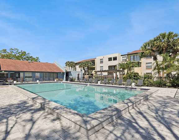A large swimming pool surrounded by a concrete patio and a building in the background.