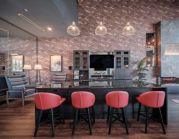 a bar with red chairs in front of a kitchen with a tv